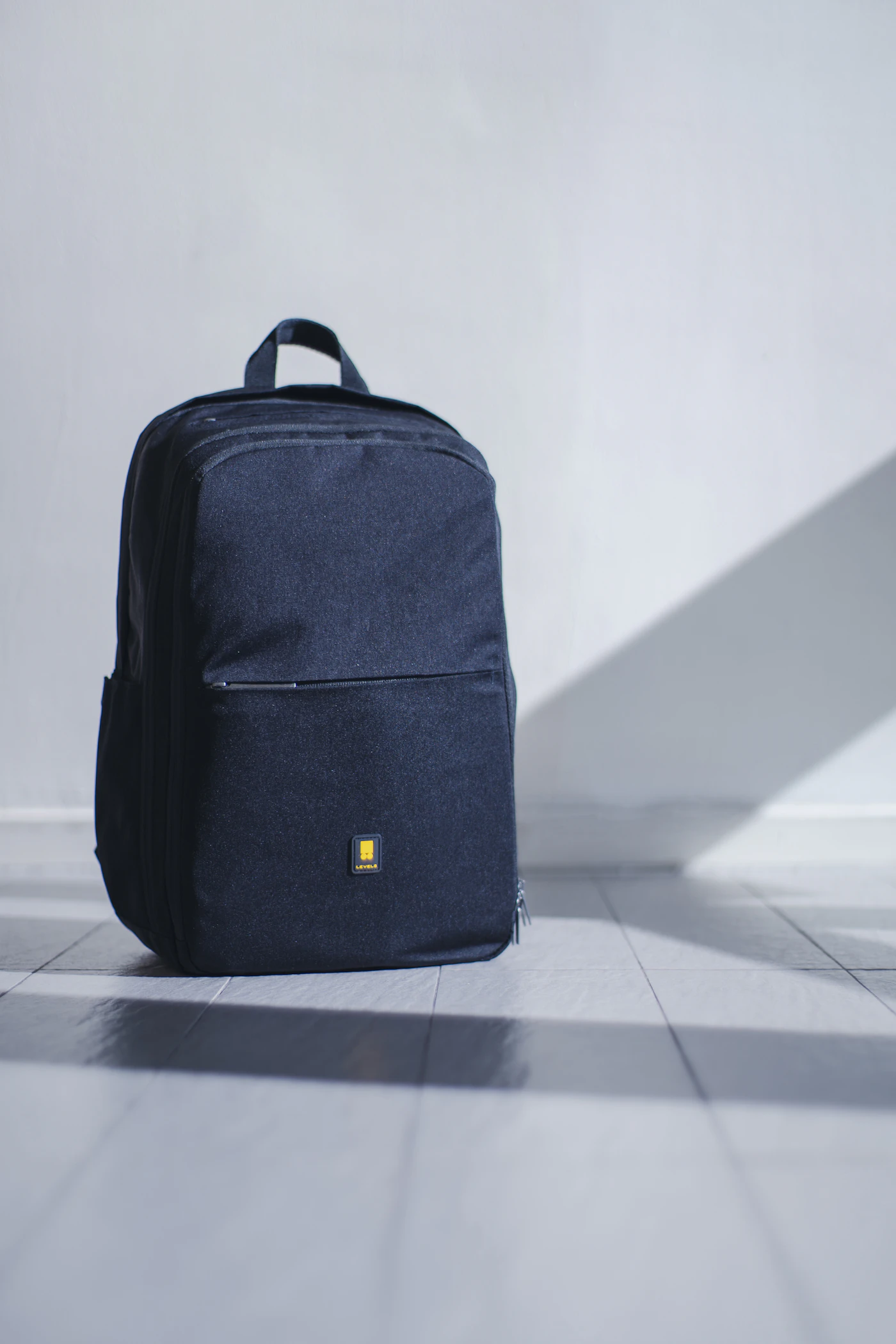 Navy backpack standing beside a pale wall